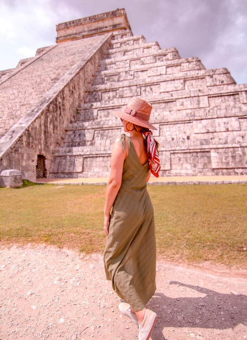 girl standing in front of Chichen Itza pyramid wearing a pink hat
