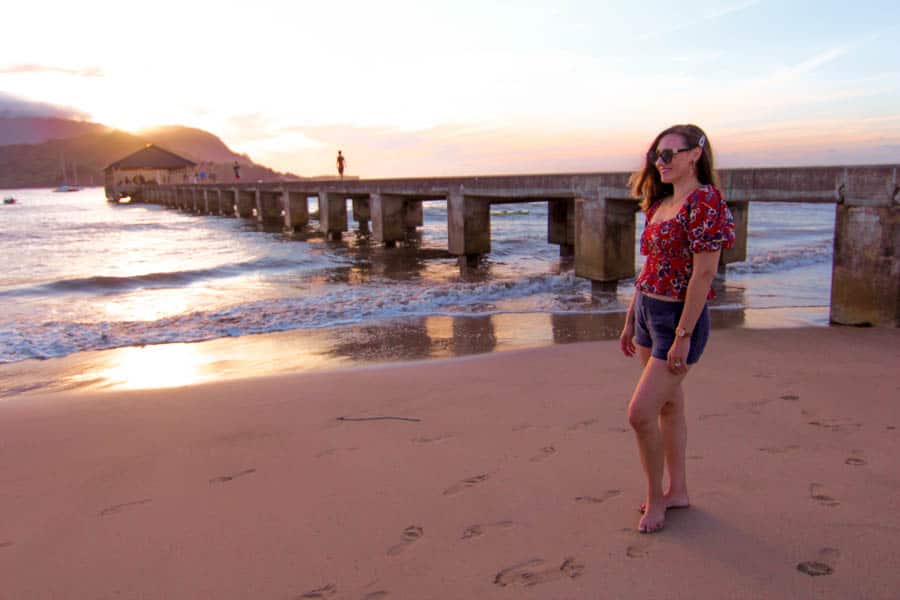 girl standing next to Hanalei pier at sunset