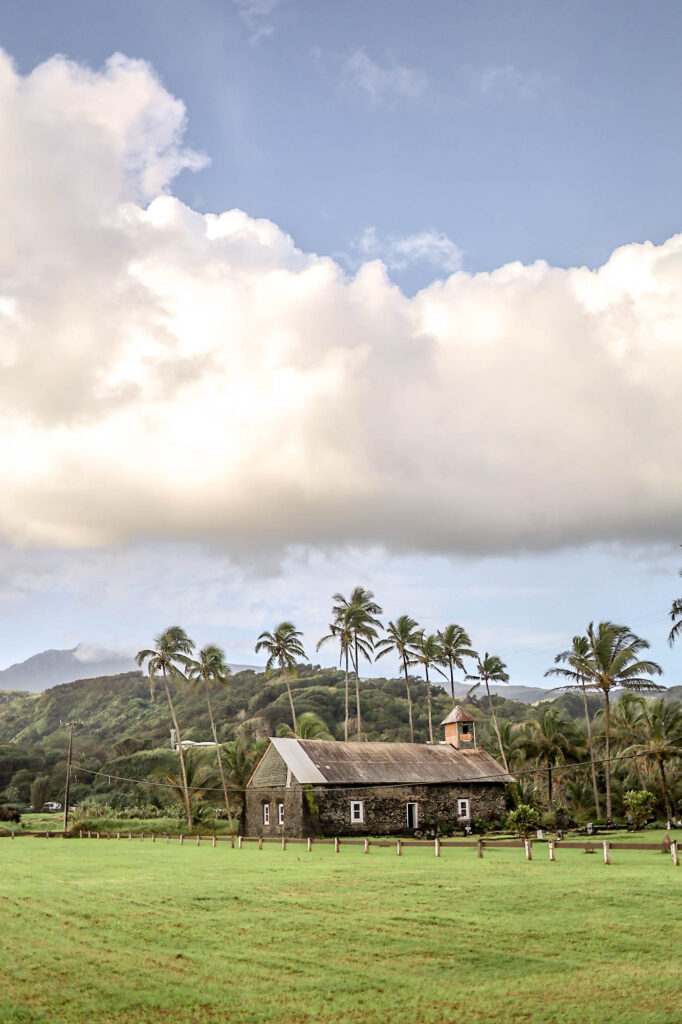 Old schoolhouse on a field with palm trees and mountains in the background KEANAE PENINSULA