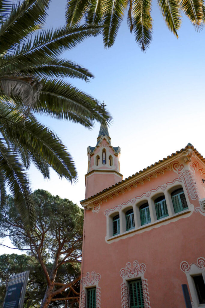 park guell pink building surrounded by palm trees in barcelona