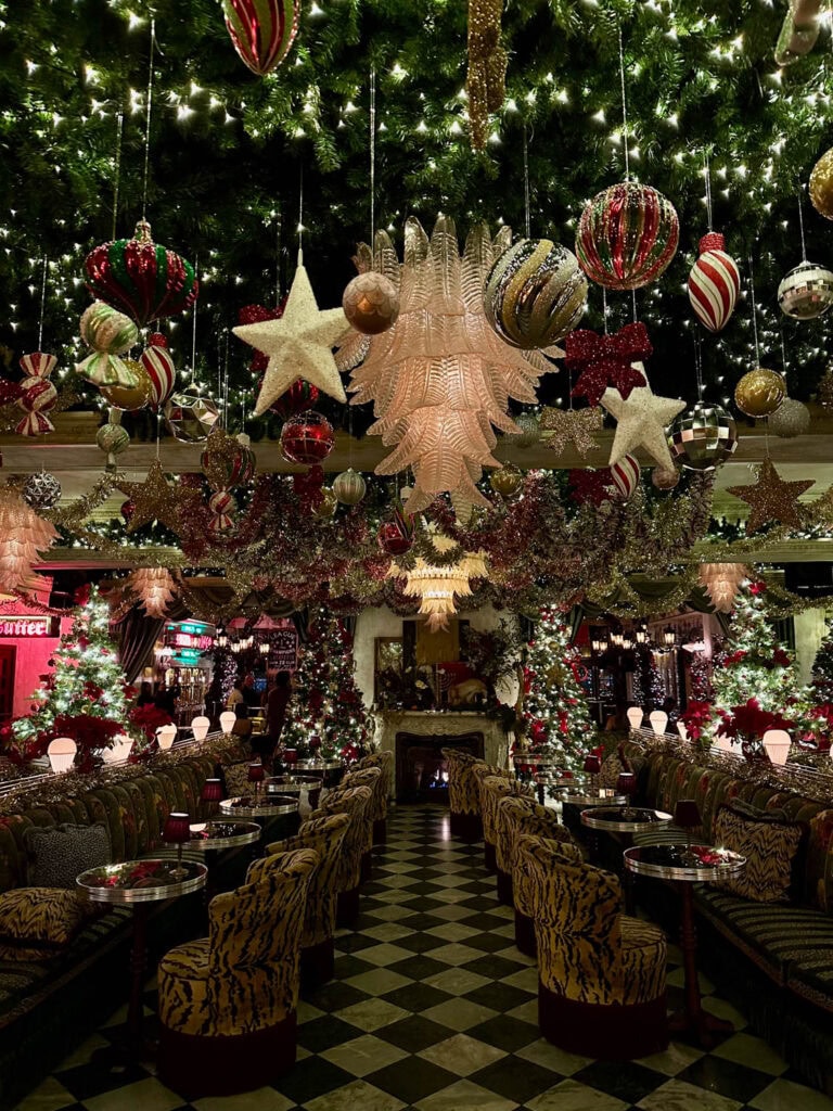 A holiday-themed hotel lounge featuring decorated trees, ornaments, twinkling lights, and cozy seating for celebration and relaxation.