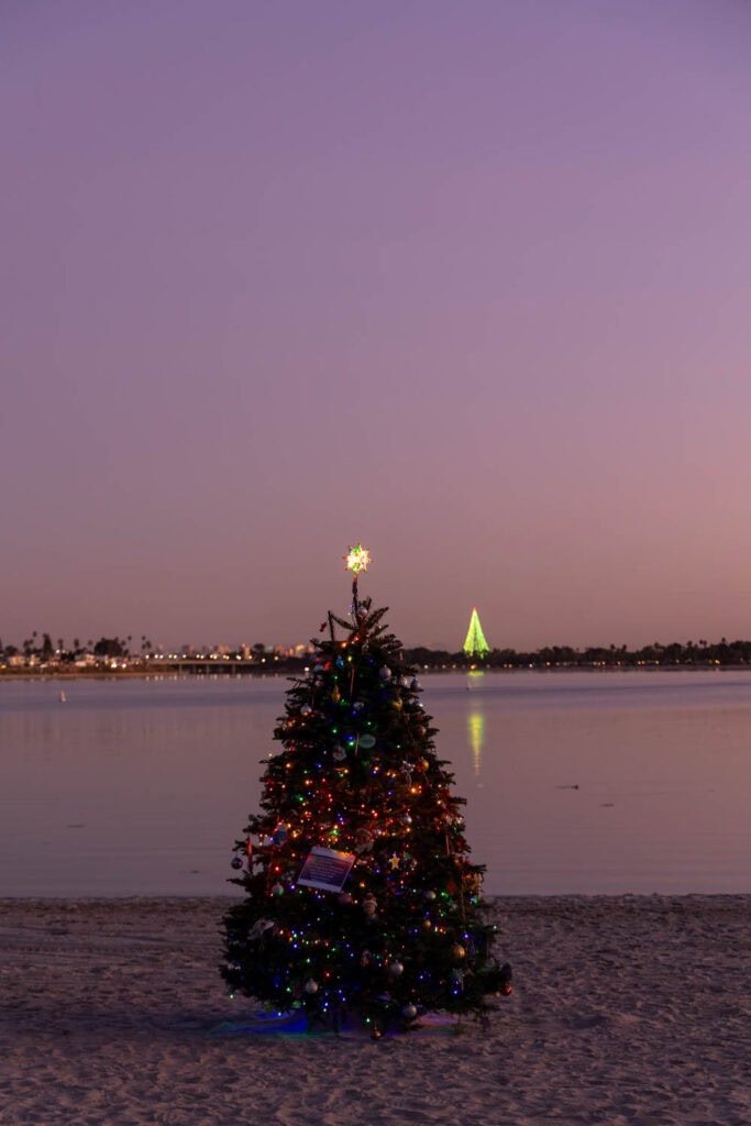 Colorful decorated Christmas tree on the beach during sunset.