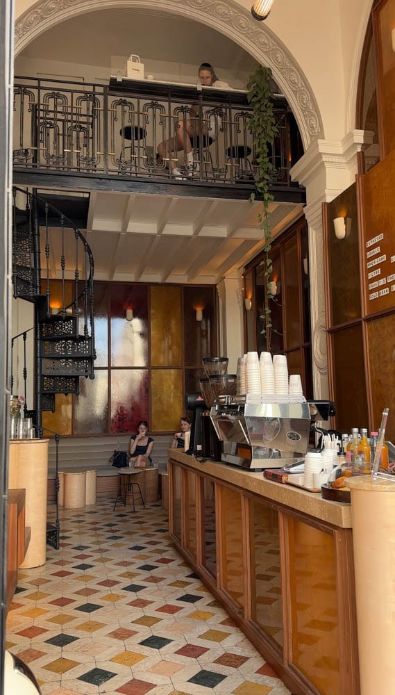 interior of two story coffee shop in paris with checkered floors, iron railing,and modern design