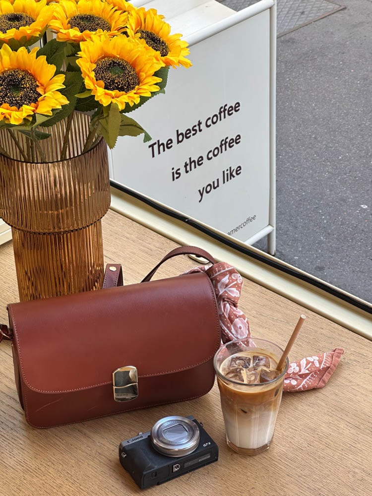 purse, camera, and latte with sunflowers at a coffee shop in Paris