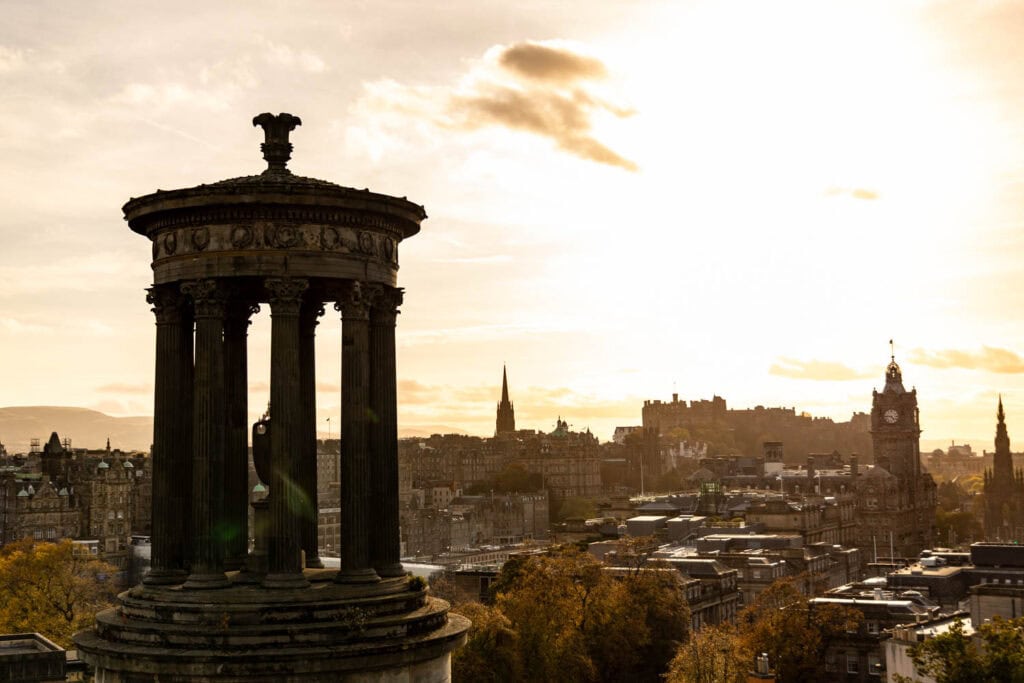 Ancient Greek-style monument overlooking Edinburgh city skyline at sunset.