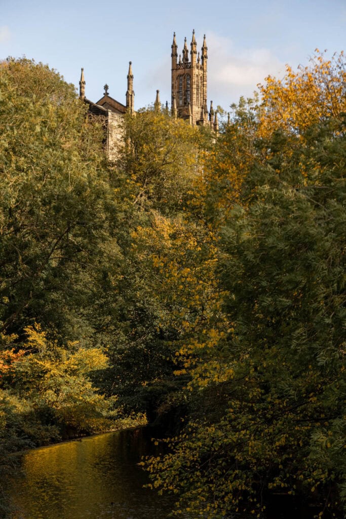 Majestic Gothic castle tower surrounded by autumn trees and a tranquil river.