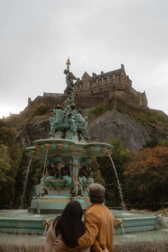 Colorful historic fountain with medieval castle in the background, tourists enjoying the scenic view in Edinburgh, Scotland.