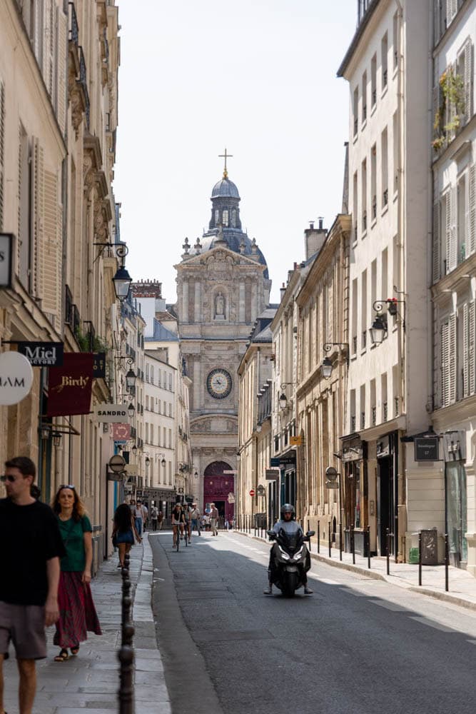 Paris street scene with historic architecture, pedestrians, and a scooter on a sunny day.