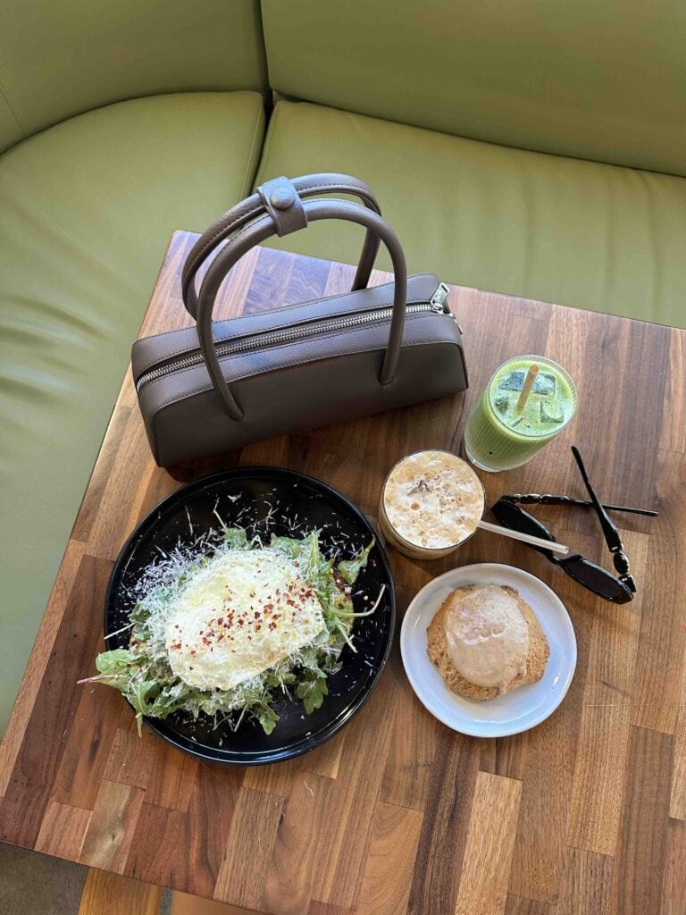 Travel meal with salad, drink, and accessories on wooden table.
