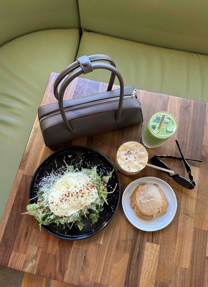 Travel meal with salad, drink, and accessories on wooden table.