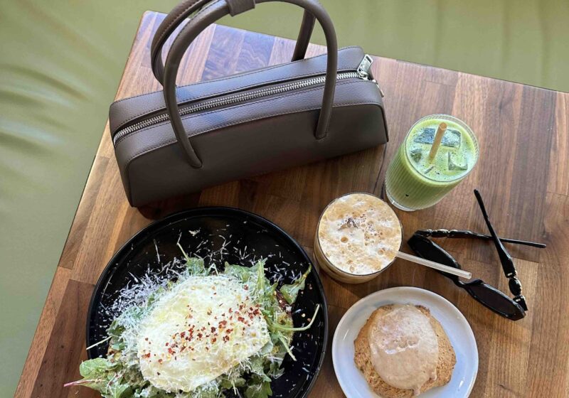 Travel meal with salad, drink, and accessories on wooden table.