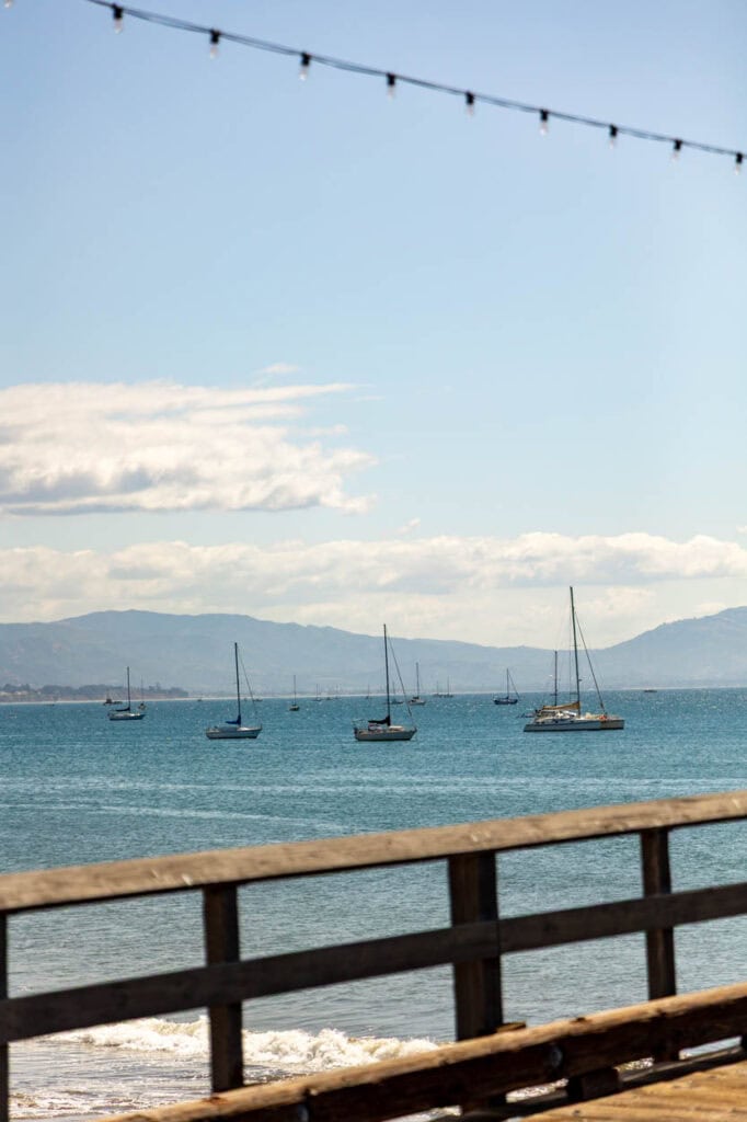 Beautiful lakeside scene featuring sailboats anchored on calm waters with mountains in the distance.