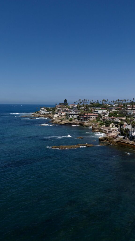 Coastal view of San Diego with ocean, cliffs, and cityscape under clear blue sky.
