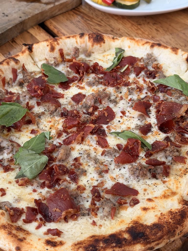 Close-up of bacon and sausage pizza with fresh basil on top.