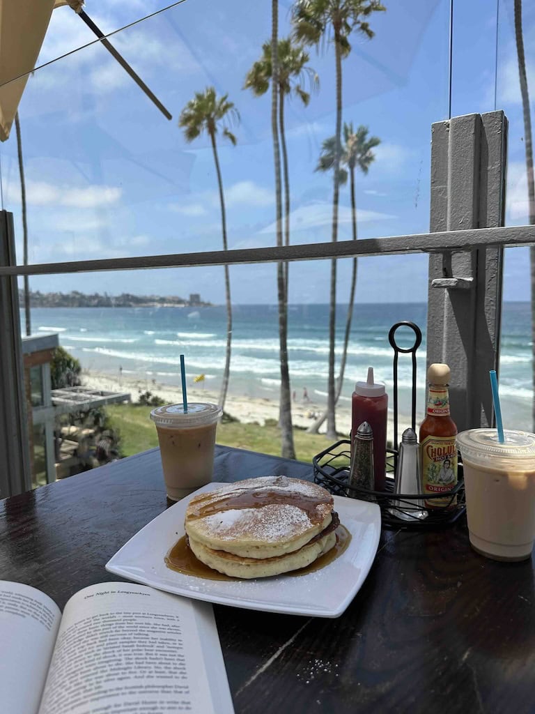Beachside breakfast with pancakes, coffee, and condiments overlooking the ocean.