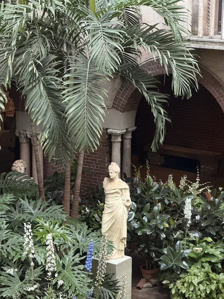 Classical statue surrounded by lush indoor plants and palm trees.