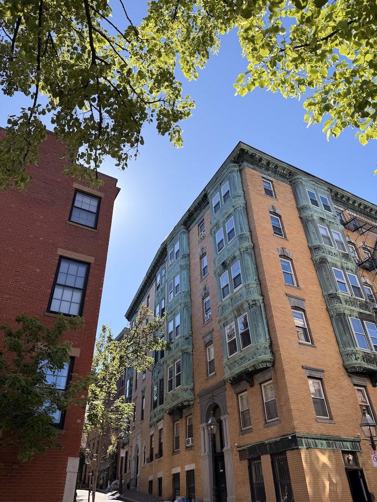 Historic brick building with bay windows and green accents in an urban setting.