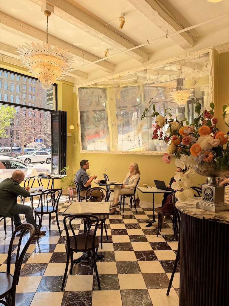Stylish cafe interior with checkered floor, large window, and floral arrangements.