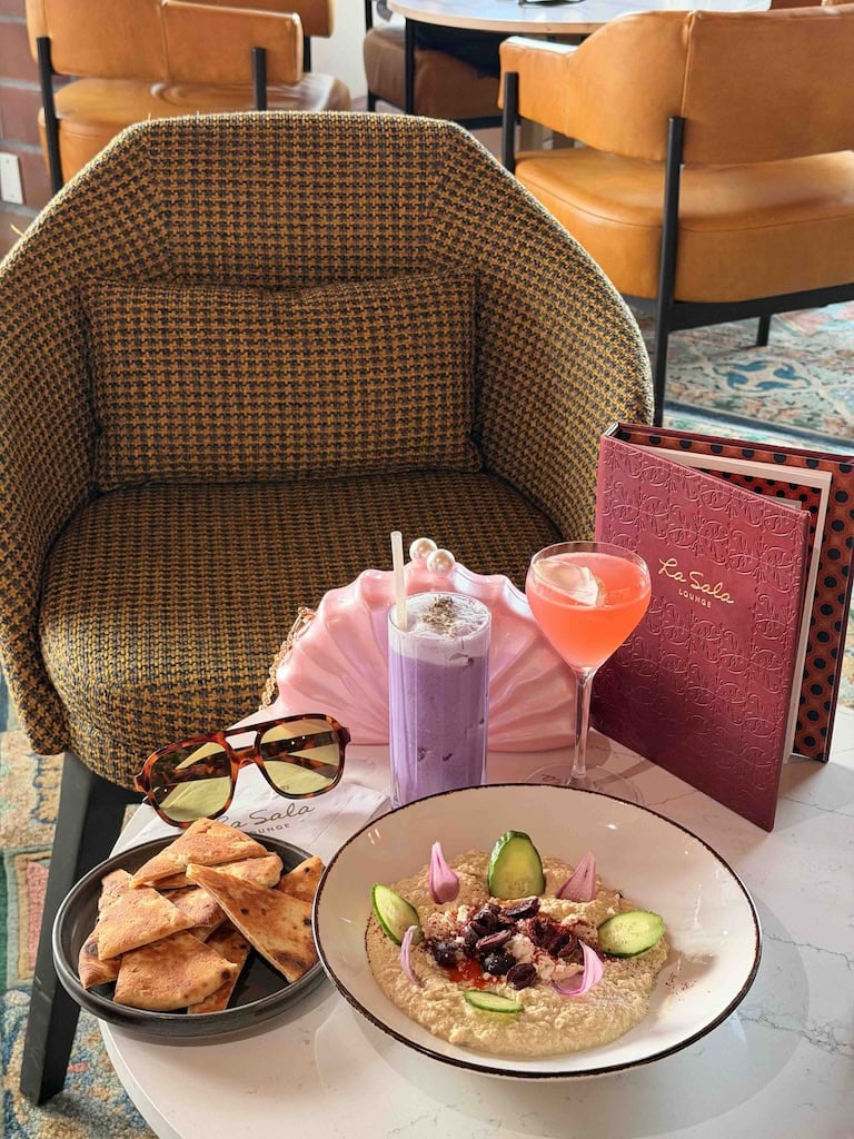 A stylish cafe table featuring vibrant beverages, snacks, sunglasses, and a menu, creating a welcoming travel-inspired ambiance.