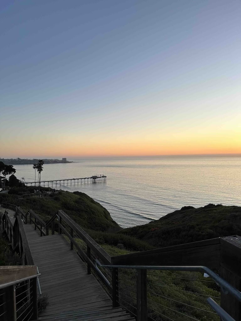 Beautiful sunset view over the ocean with a wooden pier extending into the water, surrounded by lush.