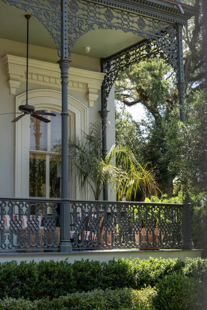 Victorian house porch with intricate ironwork and lush greenery.