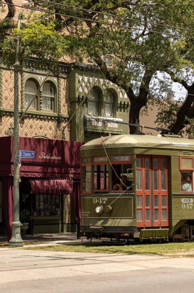 Historic green and red tram on city street with trees and buildings.