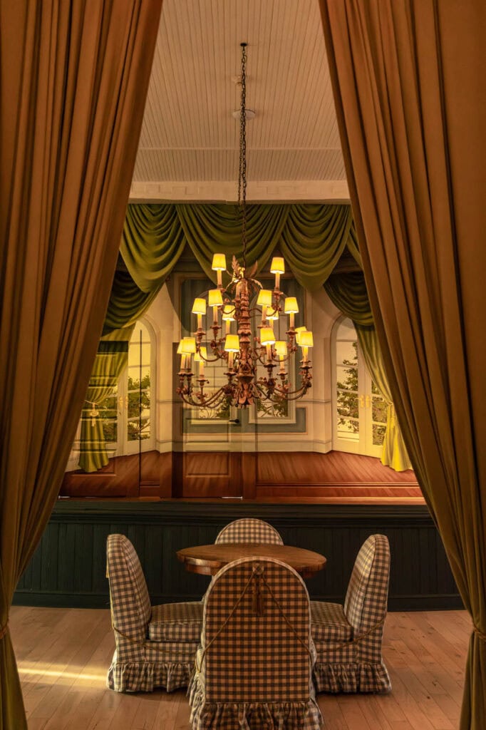 Luxurious stage with chandelier, green curtains, and a small table with chairs.