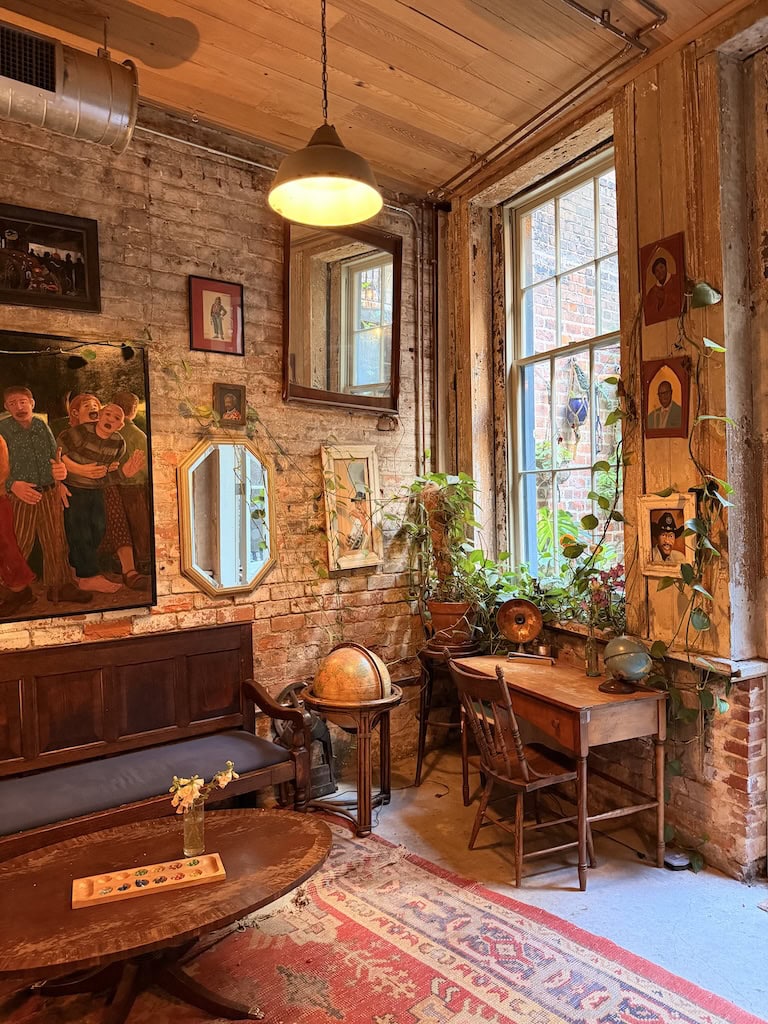 Charming vintage room with brick walls, artwork, and lush plants by the window.