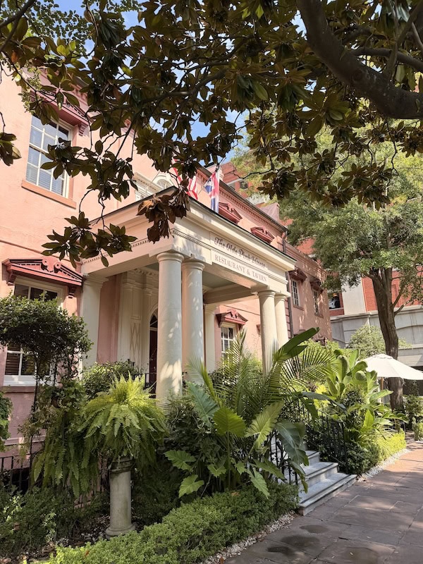 Charming boutique hotel with pink facade and lush greenery in a city setting.
