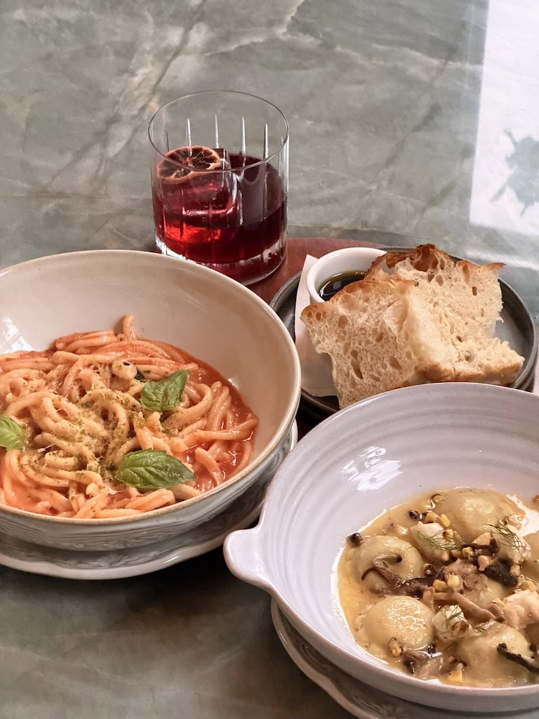 Italian pasta, bread, and soup with a glass of red wine on a marble table.