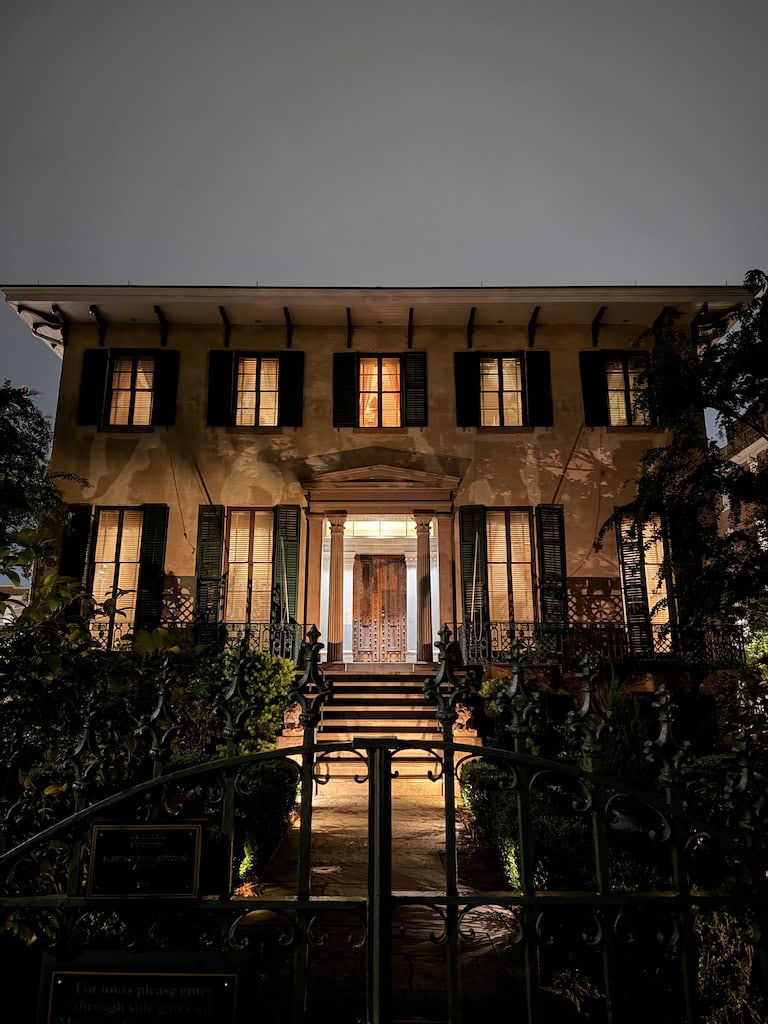 Night view of a historic house with lit windows and a garden.