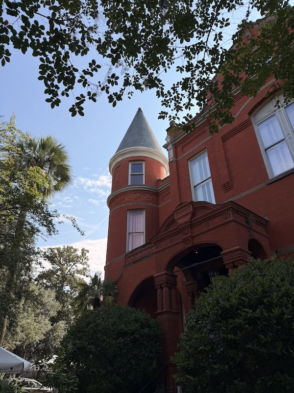 Victorian-style red brick house with turret and lush greenery.