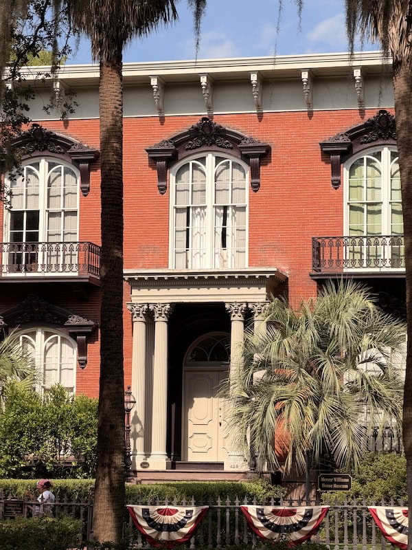 Elegant historic mansion with columns, balconies, and lush greenery.