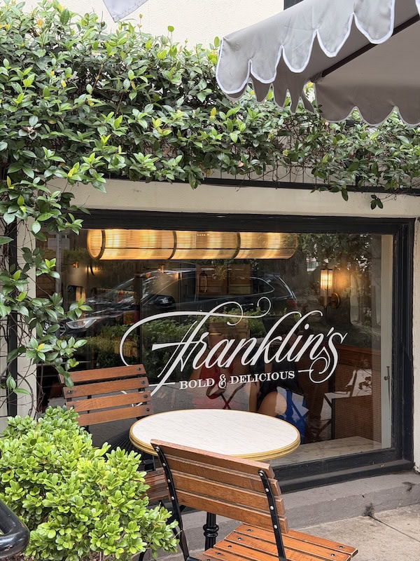 Outdoor seating at Franklin's restaurant with greenery and a window view.